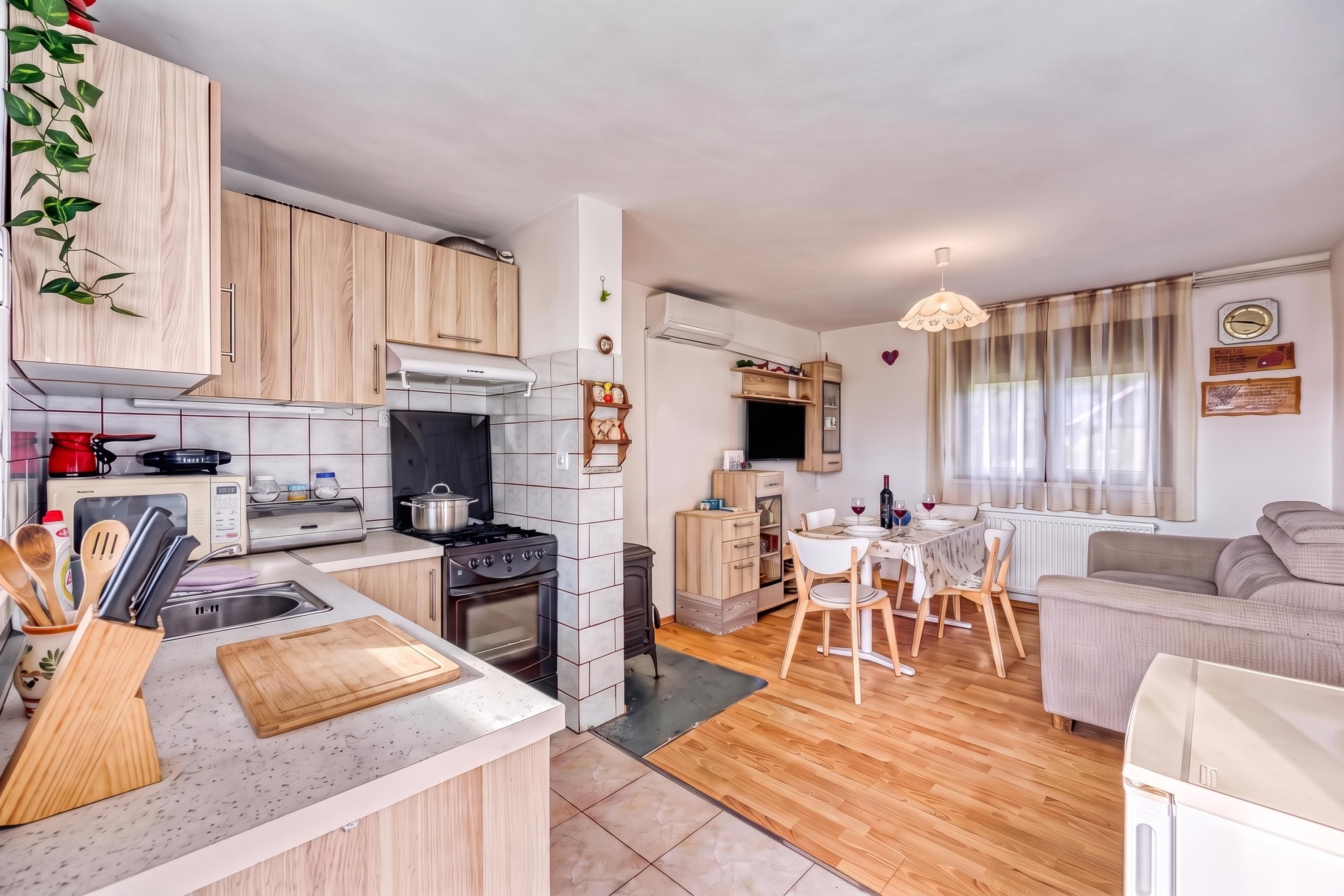 Een moderne keuken met een fornuis, magnetron en houten kasten. Er is een eethoek met een tafel en stoelen, en een zithoek met een bank.