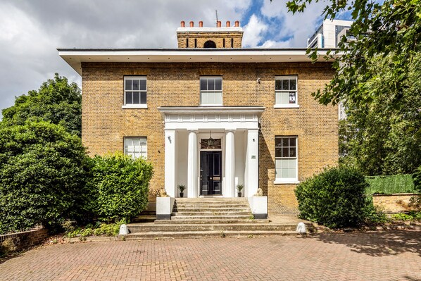 A brick building with a central entrance, flanked by two columns, and a small tower with chimneys on the roof.