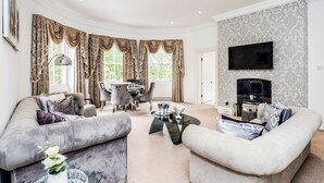 A spacious living room with a curved sofa, a glass coffee table, and a dining area with a chandelier.