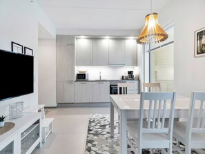 Une cuisine moderne avec des meubles blancs, une table à manger avec des chaises, un téléviseur et un luminaire suspendu.