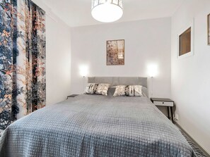 Een slaapkamer met een bed, twee nachtkastjes, een wandlamp en een raam met gordijnen.