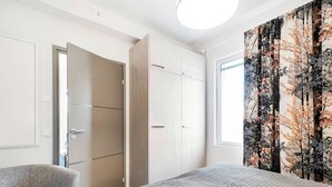 Een slaapkamer met een bed, een stoel, een kledingkast en een raam met uitzicht op bomen.