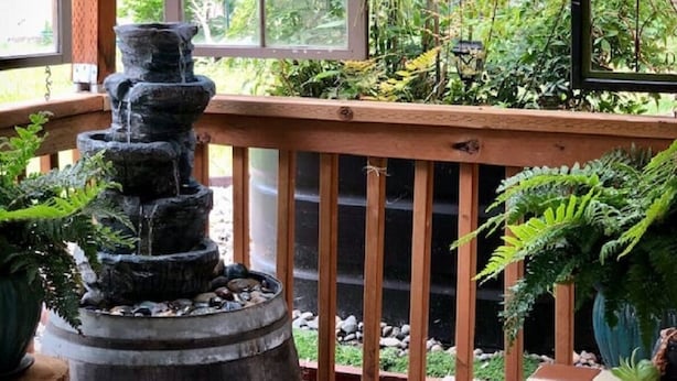 A wooden deck with a stone water feature, potted plants, and a hanging planter. - Tiny House Near Downtown Astoria (Astoria)