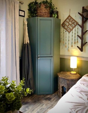 A room with a teal cabinet, a small round table with a lamp, a bed, and a plant. - Tiny House Near Downtown Astoria (Astoria)