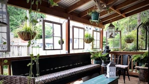 An outdoor deck with a wooden bench, wicker chairs, hanging planters, and a lantern. - Tiny House Near Downtown Astoria (Astoria)