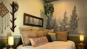 A bedroom with a large bed, multiple pillows, a wall-mounted plant, a framed picture, and two bedside tables with lamps. - Tiny House Near Downtown Astoria (Astoria)