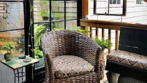 A wicker chair with a patterned cushion, a hanging plant, and a view of the outside through large windows. - Tiny House Near Downtown Astoria (Astoria)