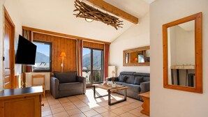 A living room with a sofa, a coffee table, a TV, and a large window with a view of mountains. - Apt CourmayeurC44 w/MontBlanc view Parking, Chamonix, France (Chamonix)