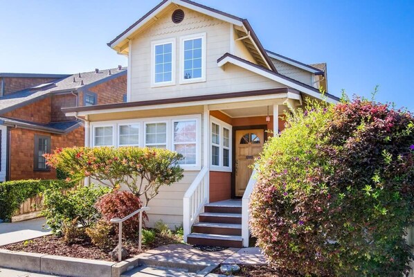 A two-story house with a front porch, a staircase leading to the entrance, and a well-maintained garden.