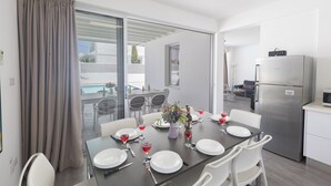 A dining area with a table set for six, a refrigerator, and a view of the outdoor pool.