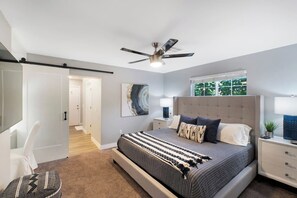 Una camera da letto moderna con un letto grande, una ventola a soffitto, un comodino e una finestra vista verde.