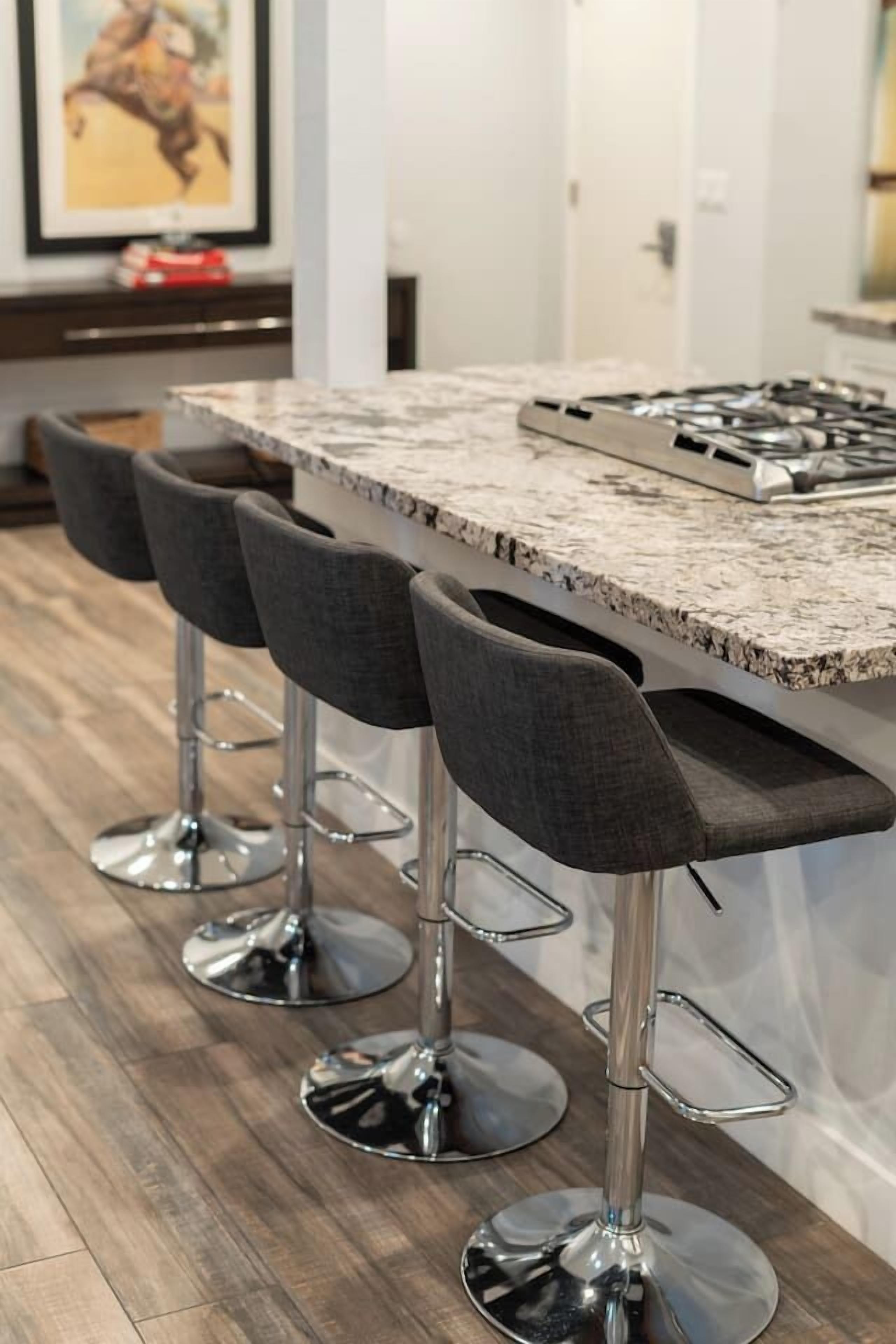 A kitchen with a marble countertop, four bar stools, and a gas stove.