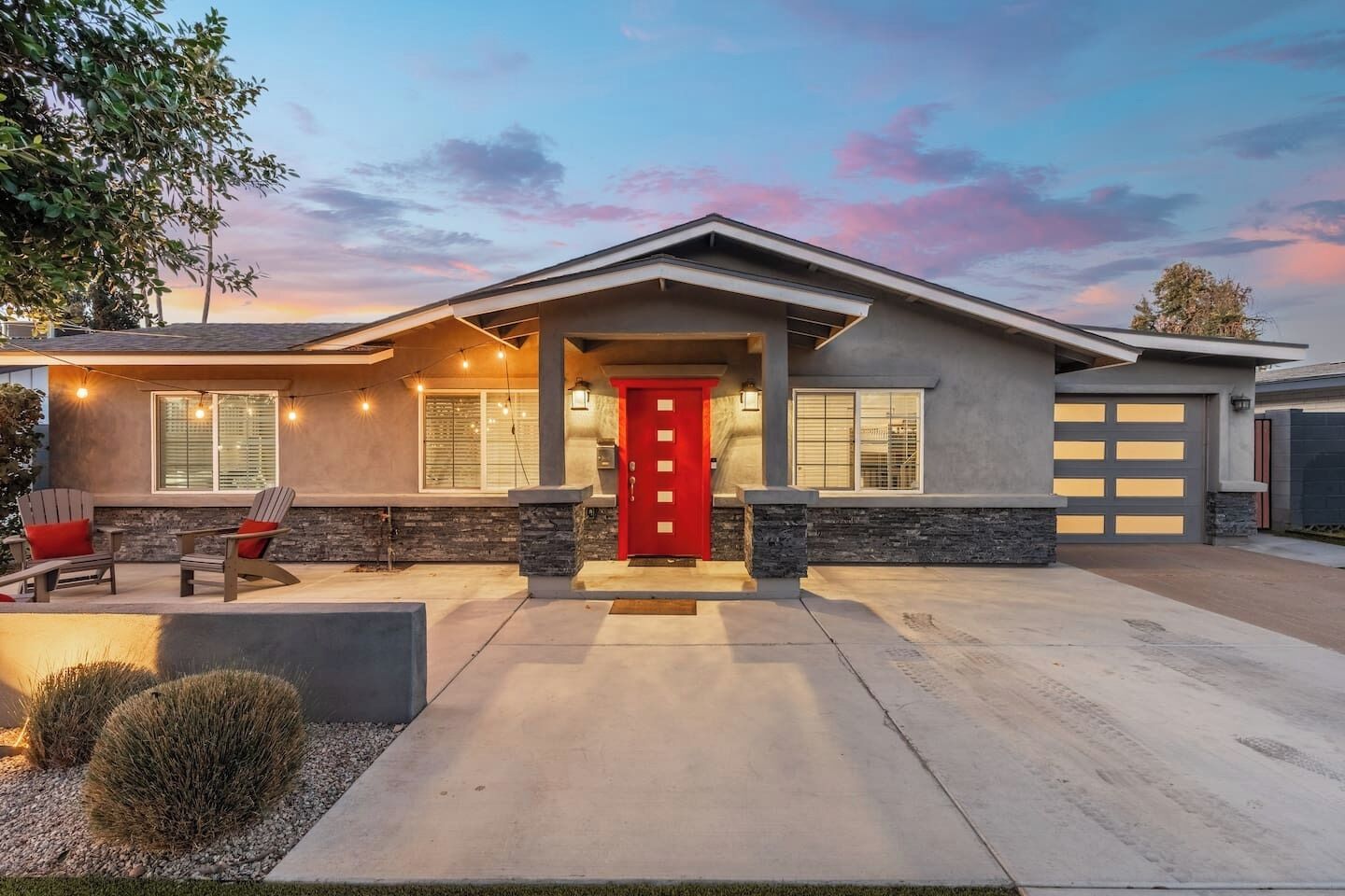 A modern house with a red door, stone accents, and a well-lit driveway.