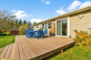 Une terrasse avec des chaises bleues et une table, une maison avec une porte-fenêtre coulissante et une cour gazonnée.