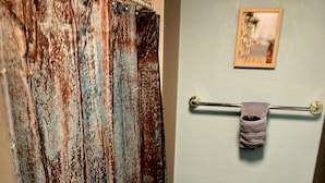 A bathroom with a rustic shower curtain, a toilet, a towel rack with a towel, and a small framed picture on the wall. - Delightful Tiny Cabin (Pikeville)