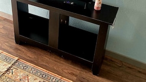 A black entertainment center with a flat-screen TV, a remote control, and a small decorative item on top. - Delightful Tiny Cabin (Pikeville)