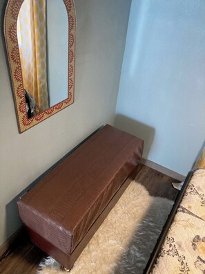 Ein kleines Zimmer mit einem Einzelbett, einem Spiegel und Holzboden.