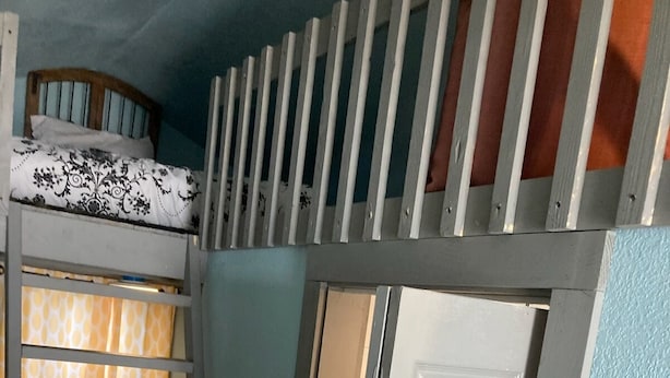 A room with a bunk bed, a door, and a window with patterned curtains. - Delightful Tiny Cabin (Pikeville)