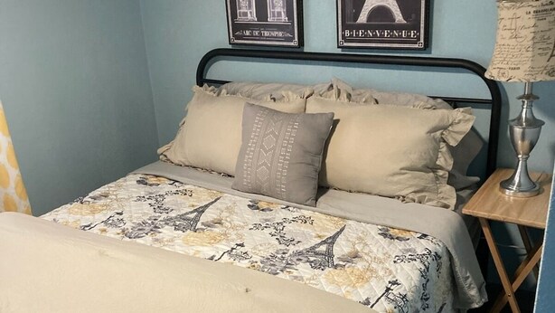 A bedroom with a bed, two pillows, a nightstand, a lamp, and two posters of the Eiffel Tower.