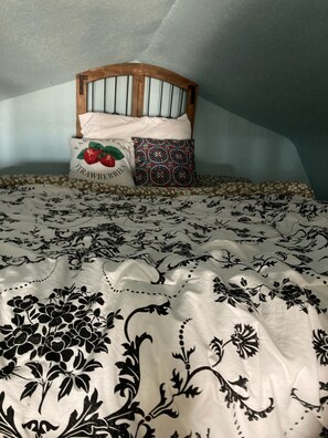 Ein Bett mit einem blumigen Überwurf, einem hölzernen Kopfteil und zwei Kissen mit unterschiedlichen Mustern.