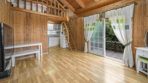 Una cabaña de madera con cocina, un comedor con banco y una puerta corrediza de vidrio a una terraza.