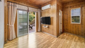 Una habitación con paneles de madera, puerta corrediza de vidrio, televisor de pantalla plana en la pared y piso de madera.