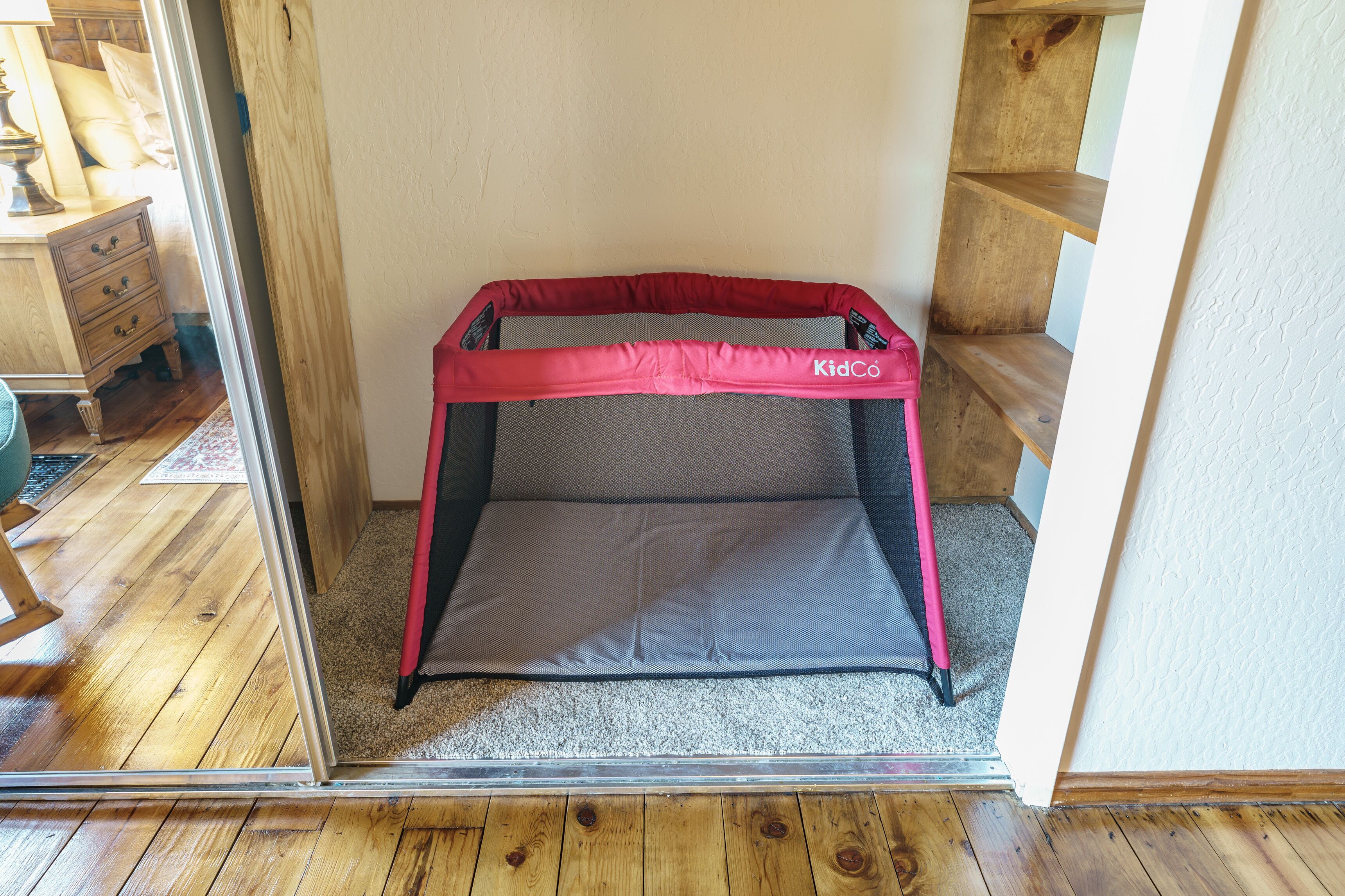 A small enclosed space with a red and black safety gate, a grey mat, and wooden flooring.