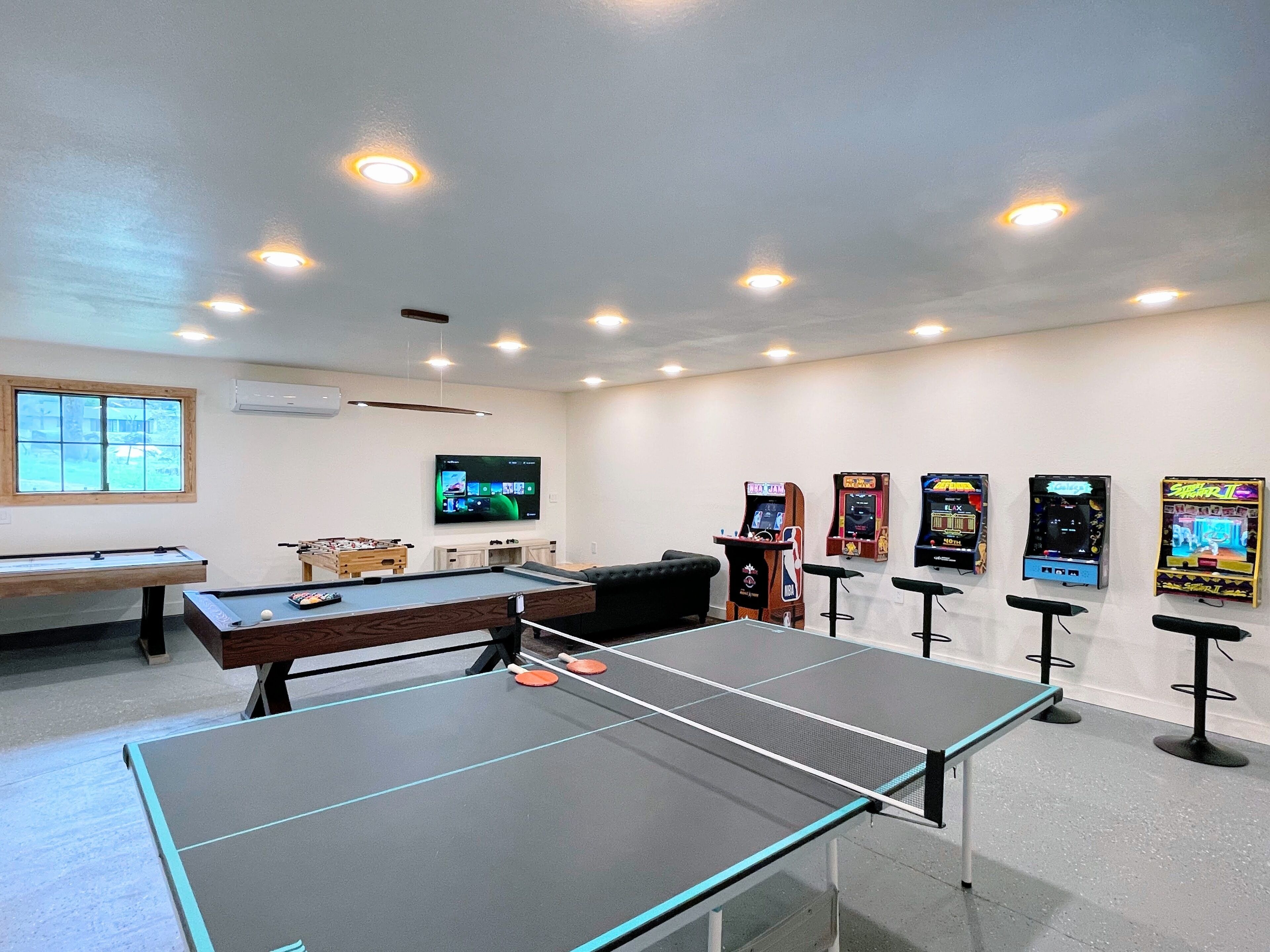 A room with a pool table, ping pong table, and several arcade games.