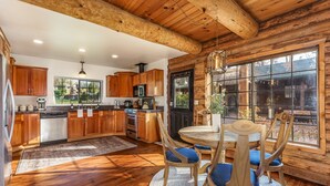 A rustic kitchen with wooden cabinets, a dining table with chairs, and a large window. - Log Cabin sleeps 20 with hot tub, EV Charger, firepit (Ahwahnee)