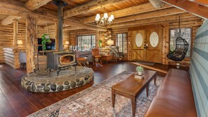 A log cabin interior with a stone fireplace, wooden furniture, and a chandelier. - Log Cabin sleeps 20 with hot tub, EV Charger, firepit (Ahwahnee)