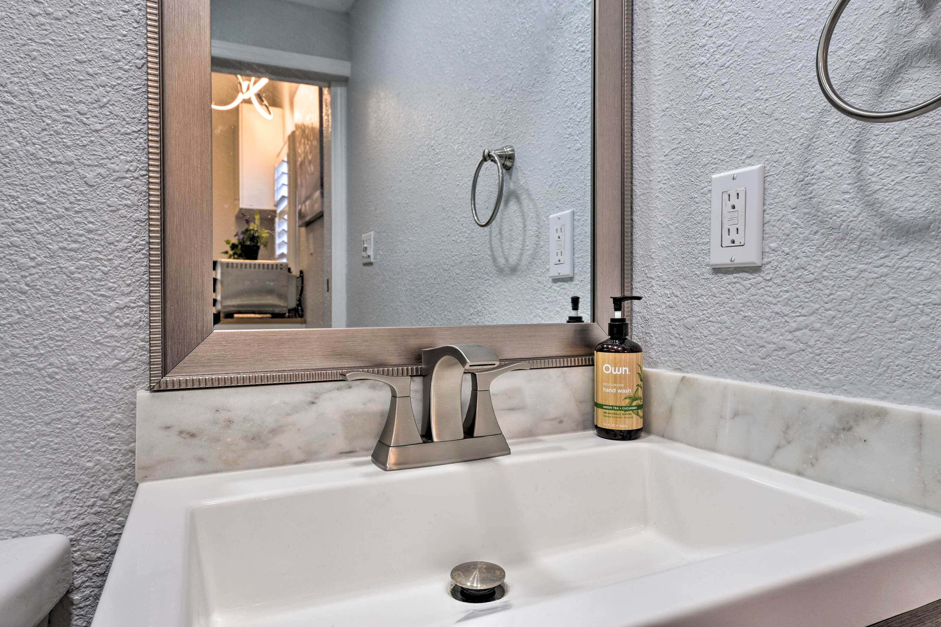 A bathroom with a white sink, a large mirror, and a hand soap dispenser.