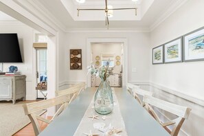 Un comedor con una mesa larga, sillas, un florero con flores y un televisor en la pared.