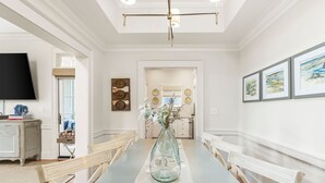 Un comedor con una mesa larga, sillas, un florero con flores y un televisor en la pared.