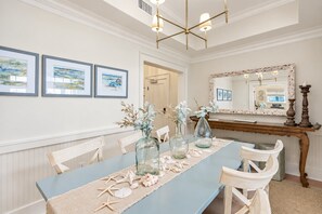 A dining area with a long table, chairs, framed artwork on the wall, and a mirror above the table. - Ave 30A - 2BR/2BA WaterColor Town Center Condo - Sleeps 4 - Beach Club Access (Santa Rosa Beach)