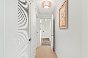 A hallway with white doors, a patterned rug, and a hanging light fixture.