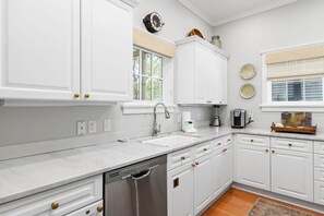A kitchen with white cabinetry, a dishwasher, a sink, and a window with blinds.