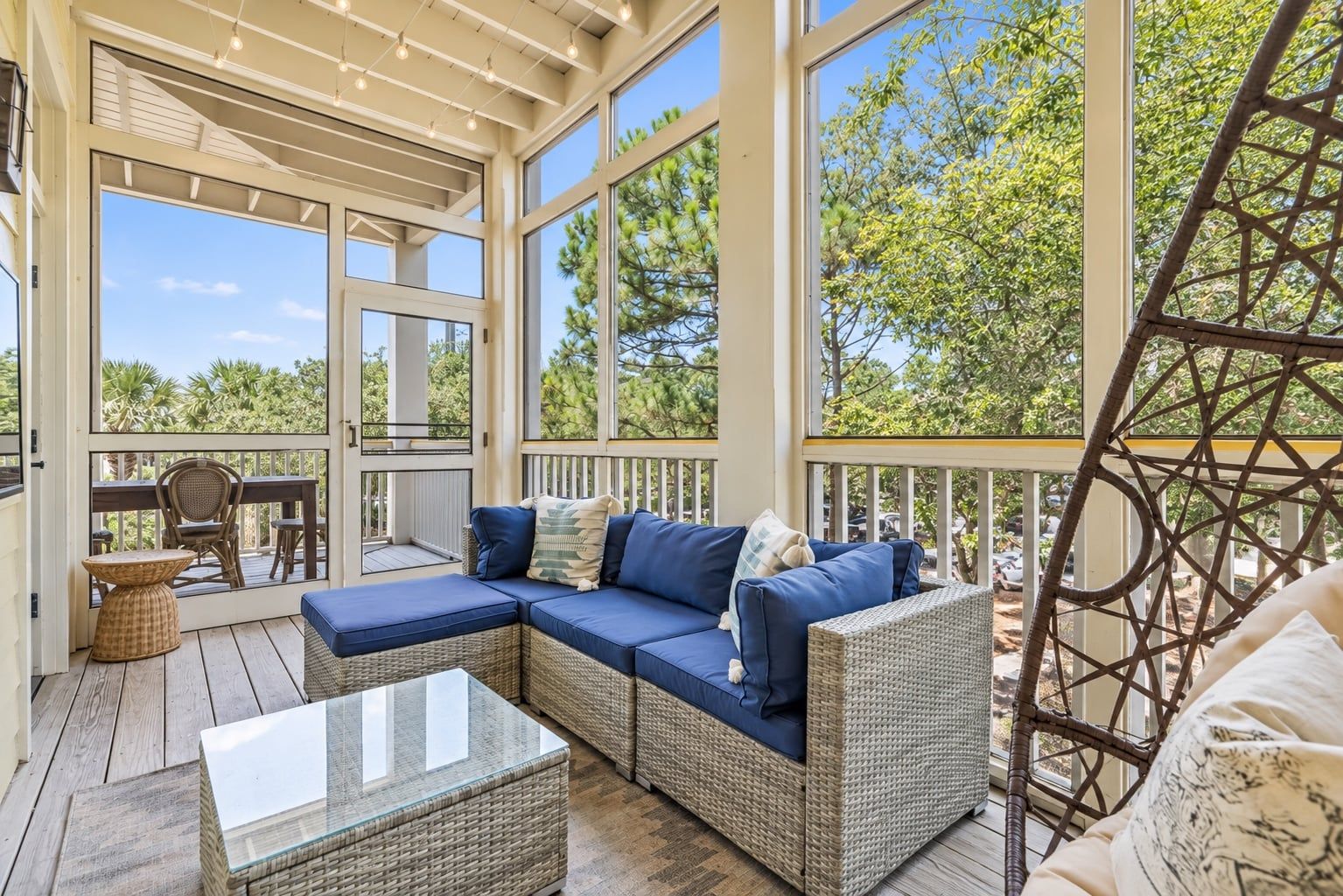 A covered outdoor area with a wicker sofa, a glass coffee table, and a wicker chair.