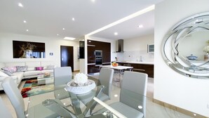 A modern living room with a glass dining table, a sofa, and a kitchen area with a microwave and oven. - Luxury condominium apartment with swimming pool (Lagos)