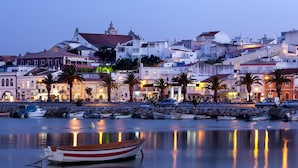 A coastal town at dusk with boats docked along the waterfront, buildings with balconies, and a prominent church spire. - Luxury condominium apartment with swimming pool (Lagos)