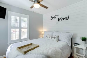 A bedroom with a bed, a ceiling fan, a window with blinds, a bedside table with a plant, and a wall with the words "Sweet Dreams!" - Step-Free Home w/ Fire Pit - 3 Miles to USC! (Columbia)
