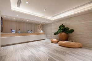 A modern reception area with a reception desk, two monitors, a large potted plant, and a wooden sculpture. - Ji Hotel (Xi'an)