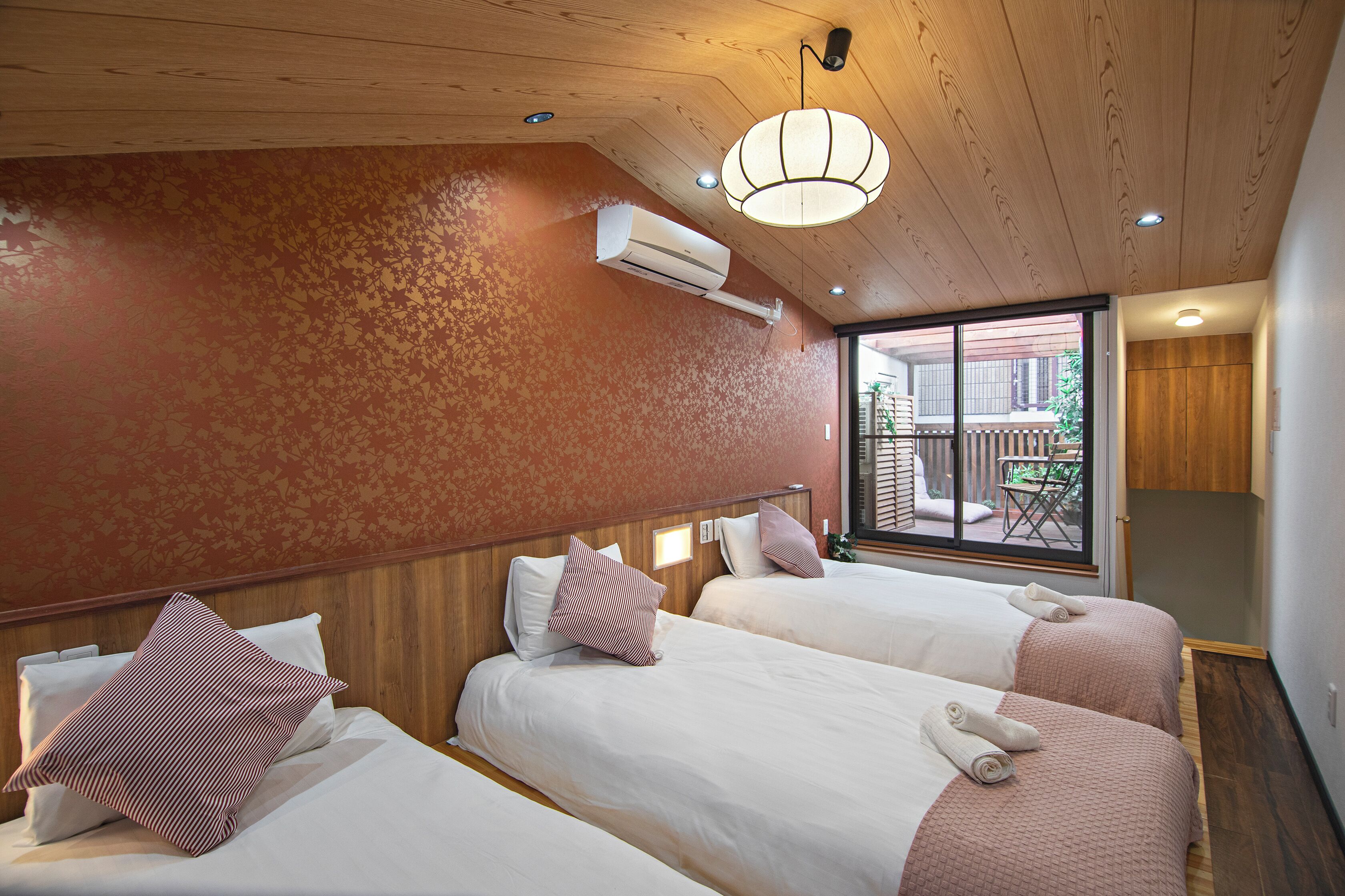 A hotel room with two beds, a wooden ceiling, an air conditioning unit, and a view of the outside balcony.