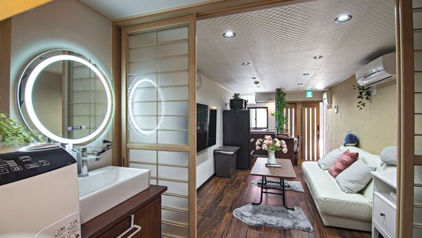 A modern hotel room with a wooden floor, a round mirror with lights, a sofa, a small table, and a washing machine. - miyu Ebisu Independent Japanese hotel (Osaka)