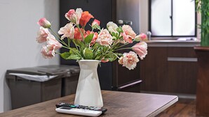A white vase with flowers on a wooden table in a room with a window and cabinets. - miyu Ebisu Independent Japanese hotel (Osaka)