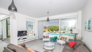 A modern living room with a sofa, armchairs, a coffee table, and a TV. There is a pool visible through the glass doors. - Protaras Holiday Villa Ccv2 (Protaras)