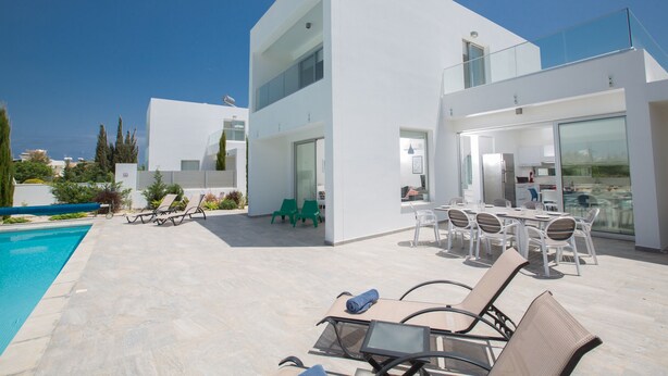 A modern, multi-story building with a pool, outdoor seating, and a glass balcony. - Protaras Holiday Villa Ccv2 (Protaras)