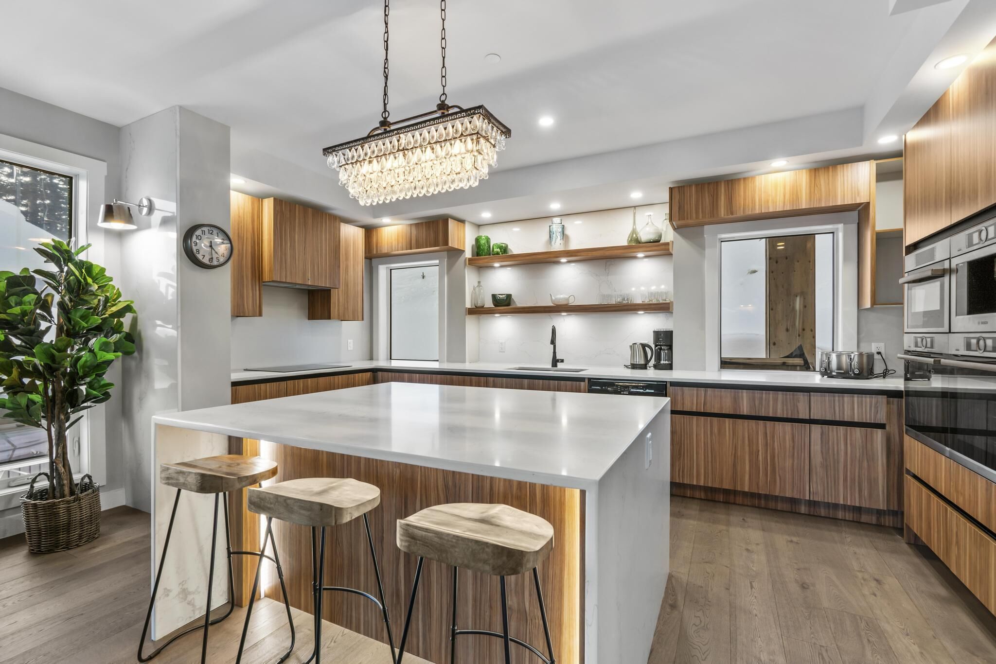 A modern kitchen with a central island, wooden cabinets, stainless steel appliances, and a chandelier.