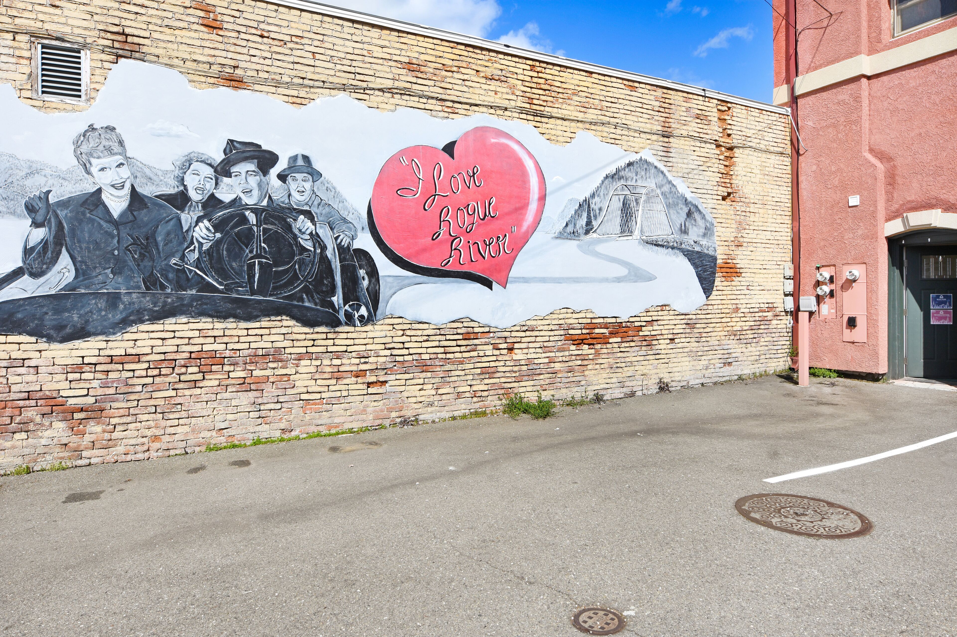 A mural on a brick wall depicting a group of people and a heart with the text "I Love Rogue River".