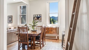 Un espace repas avec une table et des chaises en bois, un ventilateur de plafond et une vue sur l’extérieur grâce à une grande fenêtre.