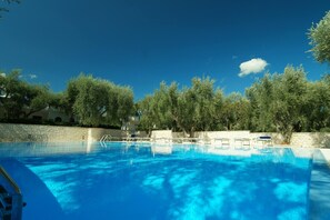 Una piscina con agua azul cristalina, rodeada de árboles y un muro de piedra.